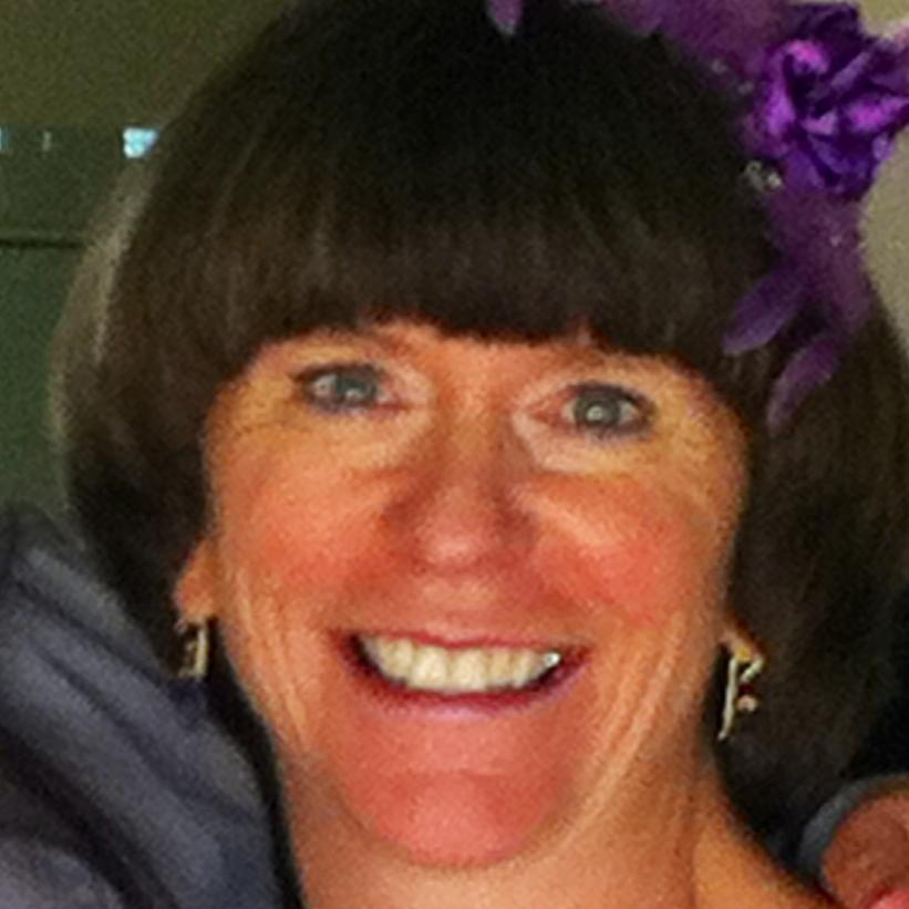 SAIL Board member Mary Gregg, smiling with a purple flower in her short dark brown hair.