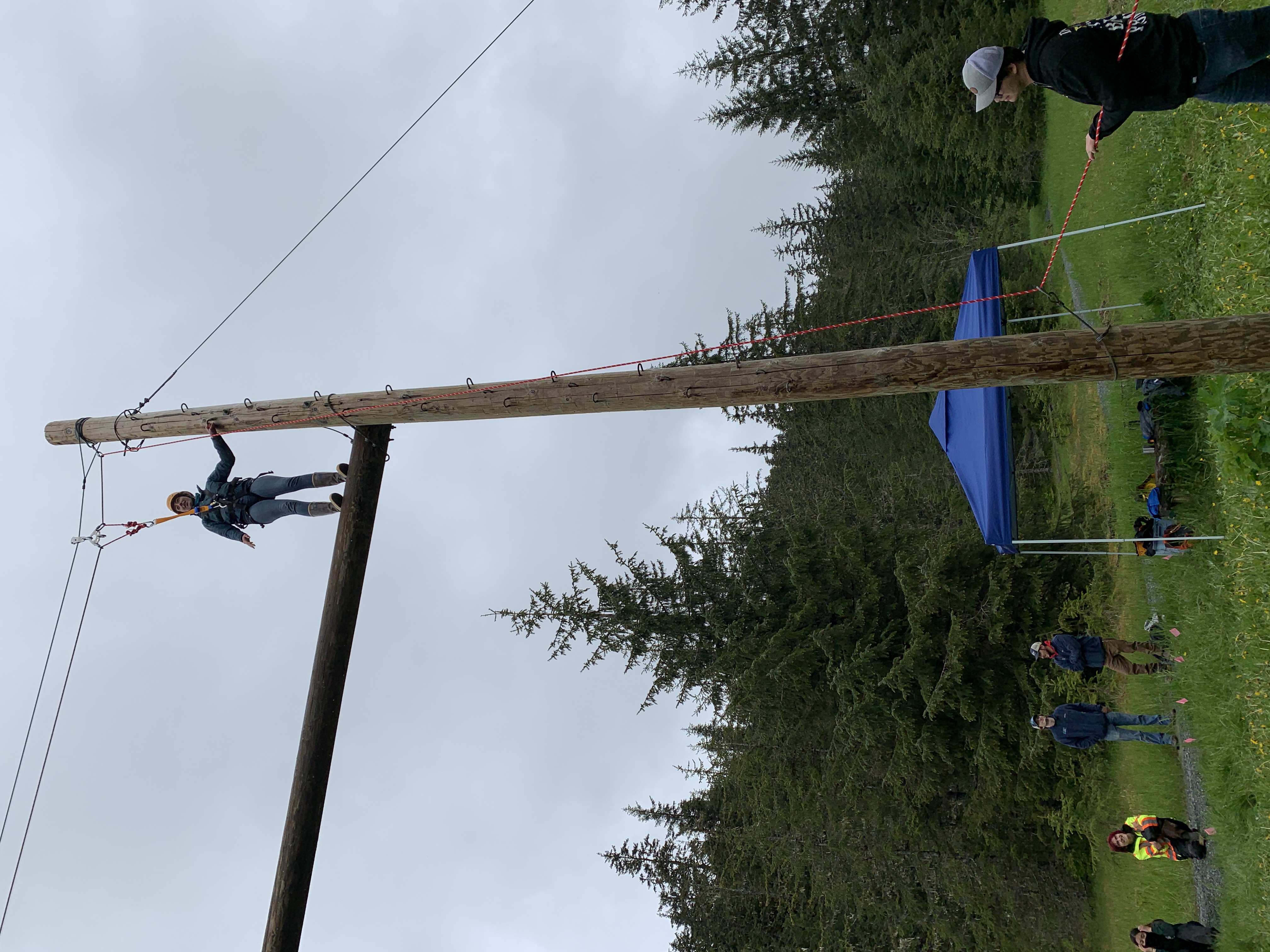 a young man standing atop a horizontal pole hung between two, very tall telephone poles