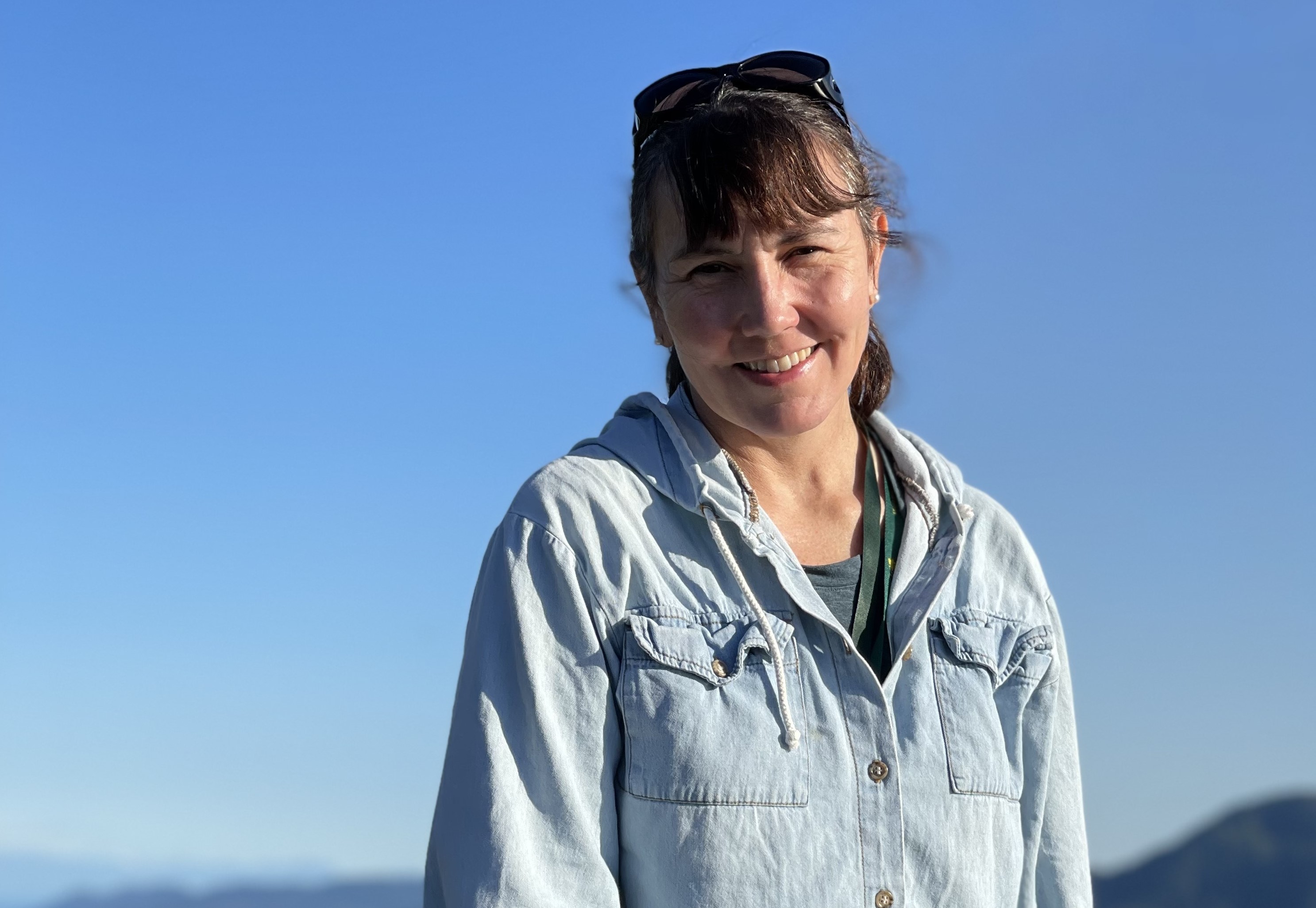 closeup of linda smiling, sunglasses on head, blue sky in background