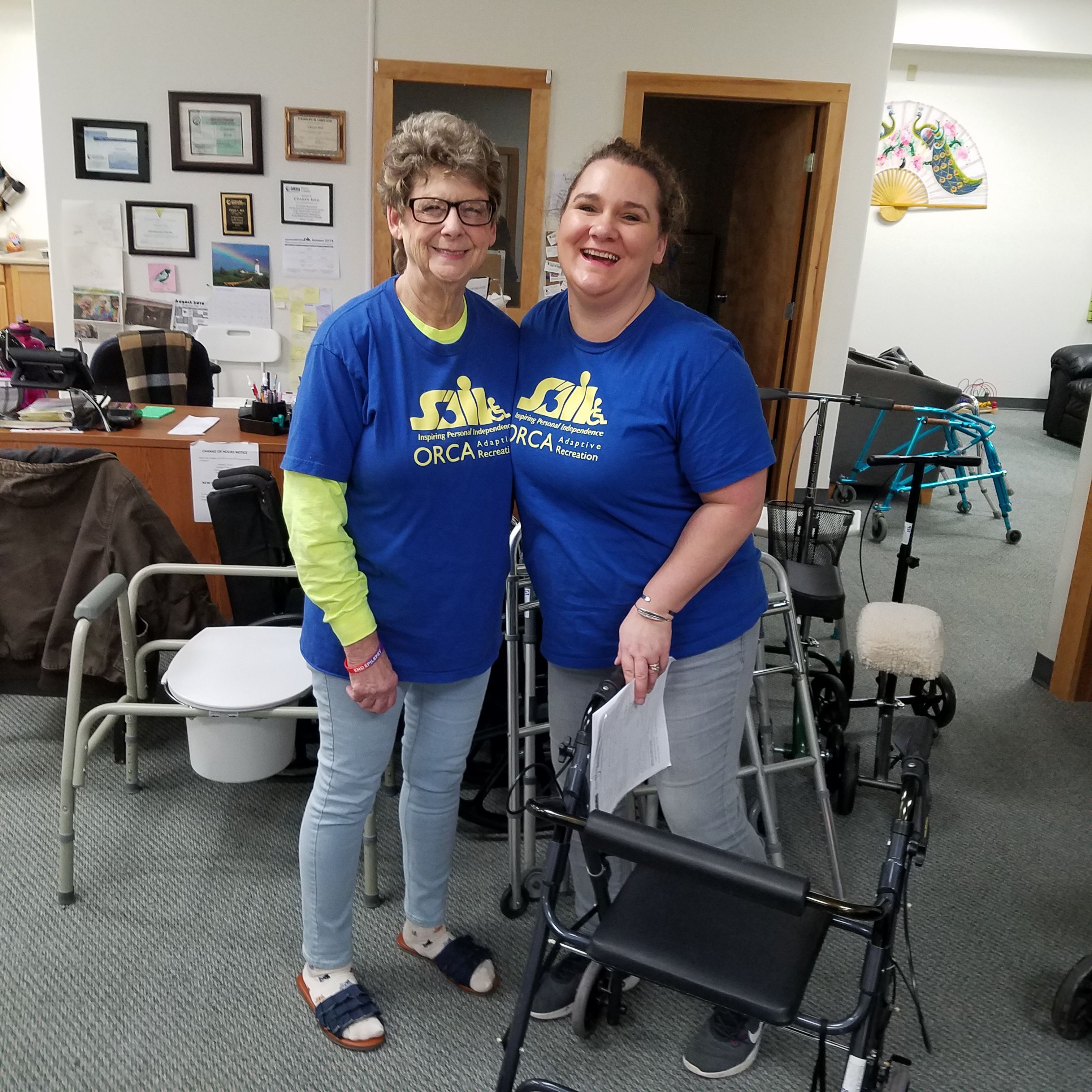 Pg16 MelissaBirdie loan closet two women, wearing blue shirts with a yellow SAIL logo, smiling while standing amidst various durable medical equipment items