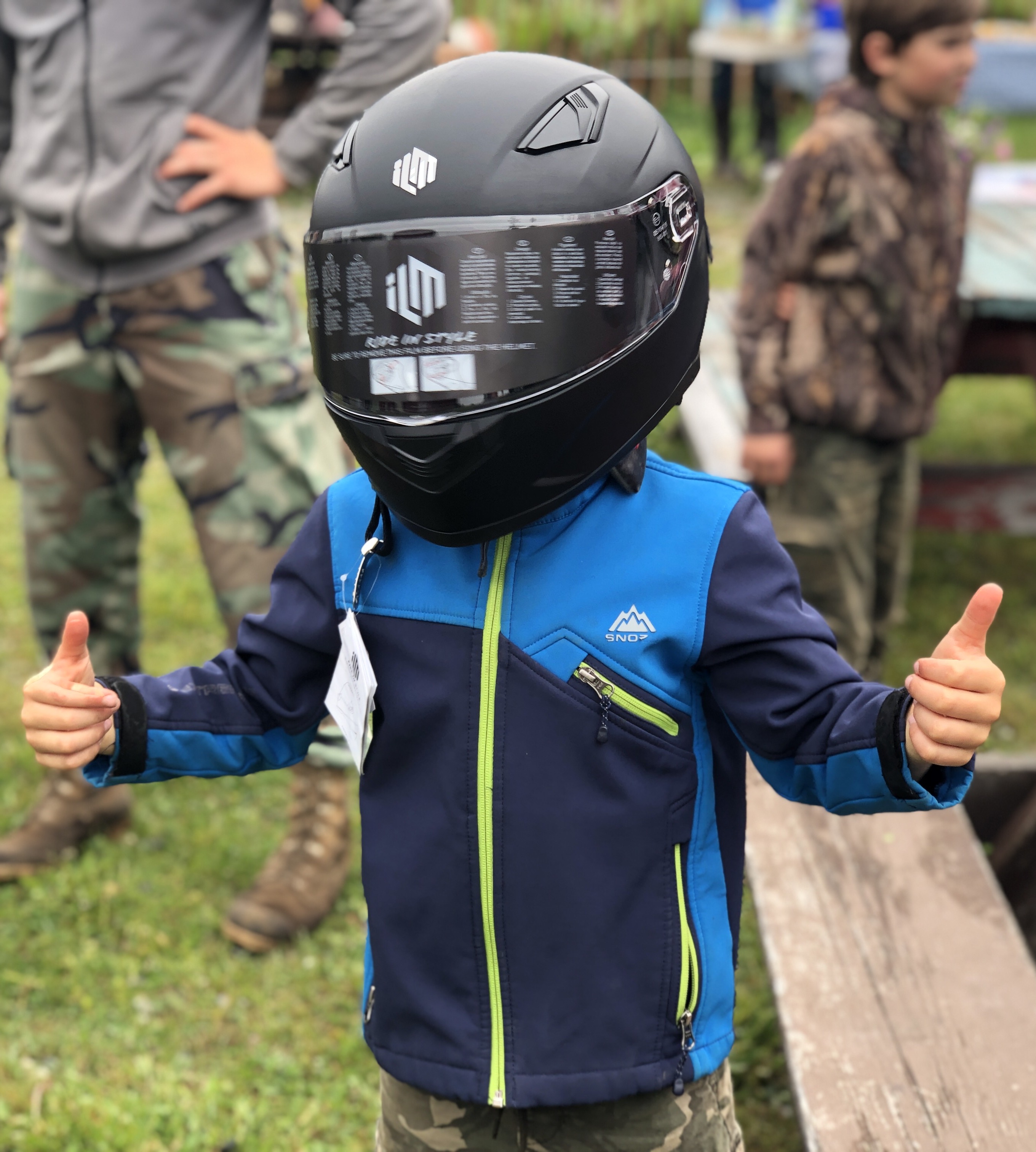 a little boy in a blue jacket wearing an atv helmet giving the thumbs up