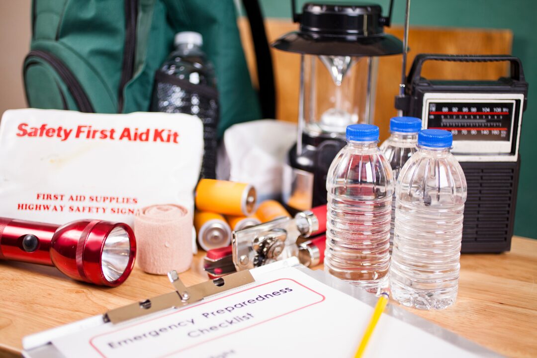items that are useful in a home emergency kit, including water bottles, flashlight, first aid kit, lantern, batteries, and a radio.